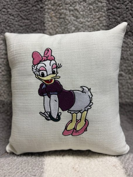 A decorative cushion featuring a cartoon character of a duck wearing a bow and sweater.