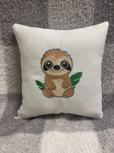 Cute sloth sitting on leaves, embroidered on a decorative cushion.