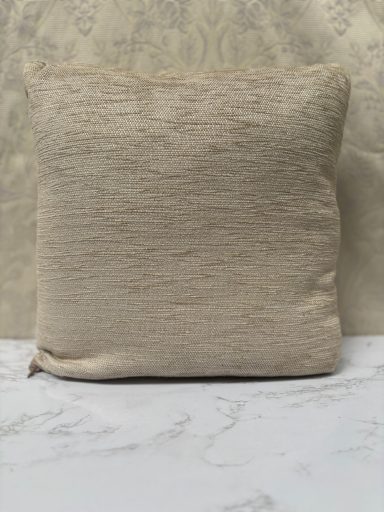 Plain beige cushion with a textured surface, resting on a marble-like surface.