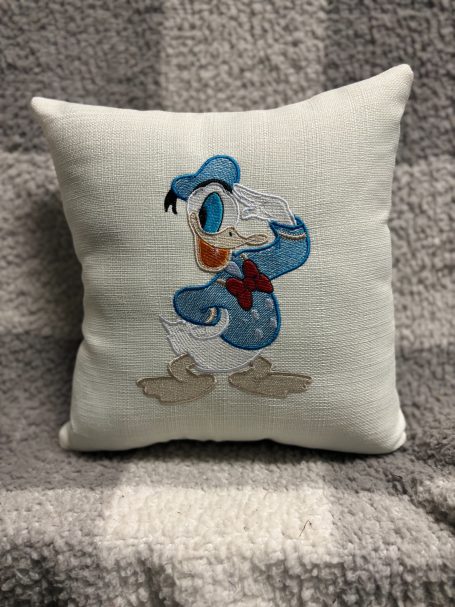 A decorative pillow featuring an embroidered Donald Duck design.