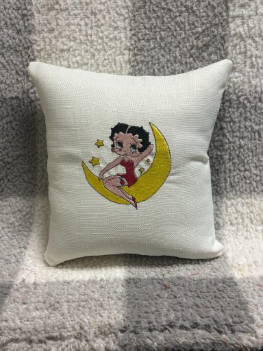 A cushion featuring a cartoon character sitting on a yellow crescent moon.