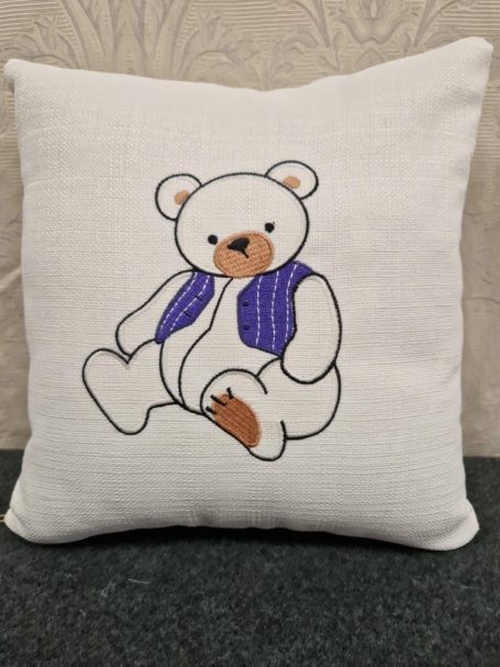 A decorative cushion featuring a cartoon bear in a blue vest.