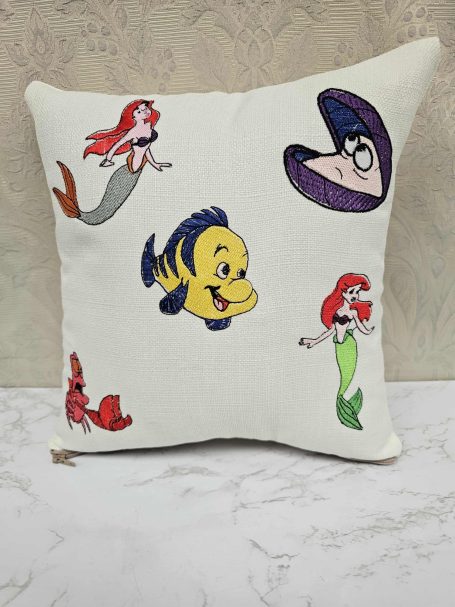 Cushion featuring characters from "The Little Mermaid," including Ariel and Flounder.