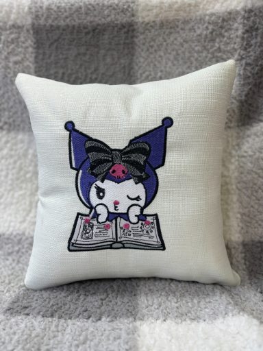 Cute cushion featuring a cartoon character with a bow, reading a book.