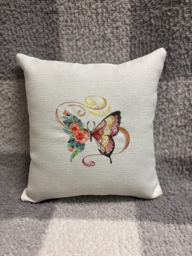 Cushion with a butterfly and floral embroidery on a textured background.