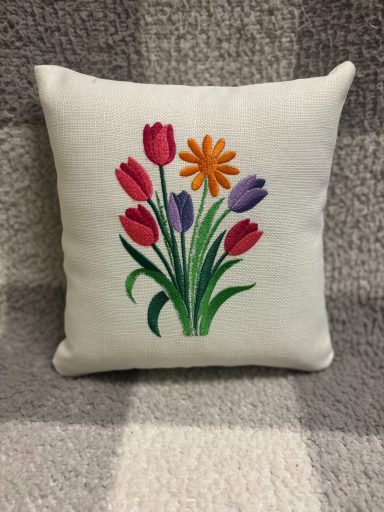 Cushion with an embroidered bouquet of red, purple, and orange flowers.