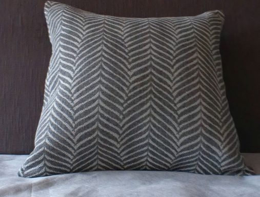 Square cushion with a grey and white chevron pattern on a dark background.