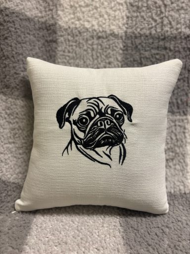 A small cushion featuring a black illustration of a pug's face.
