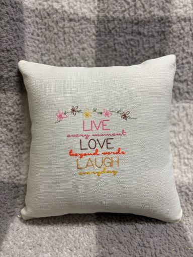 A decorative cushion with the phrases "Live", "Love", and "Laugh" in vibrant colours.