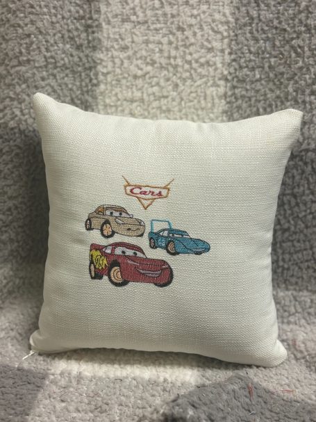 Cushion featuring cartoon cars from the movie 'Cars' embroidered on a white background.