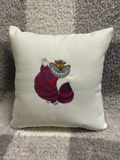 A decorative cushion featuring a whimsical cat design with a mischievous smile.