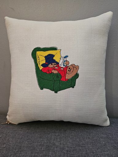 A decorative cushion featuring a bear and a character relaxing on a green armchair.