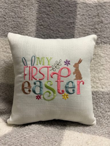 Decorative cushion with "My First Easter" text and bunny design on a patterned background.