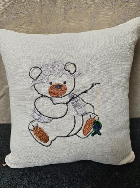 A decorative cushion featuring an embroidered bear holding a fishing rod.