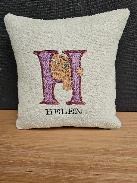 Cream cushion with a large embroidered purple "H" and the name "HELEN" underneath.