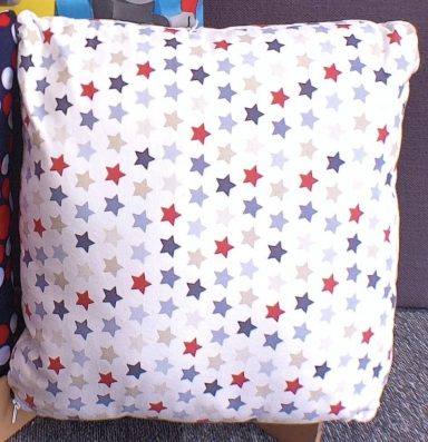 Square cushion covered in a patterned fabric of red, blue, and beige stars.