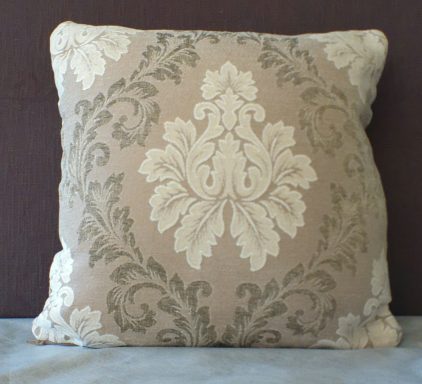 Decorative square cushion with an ornate cream floral pattern on a light brown background.