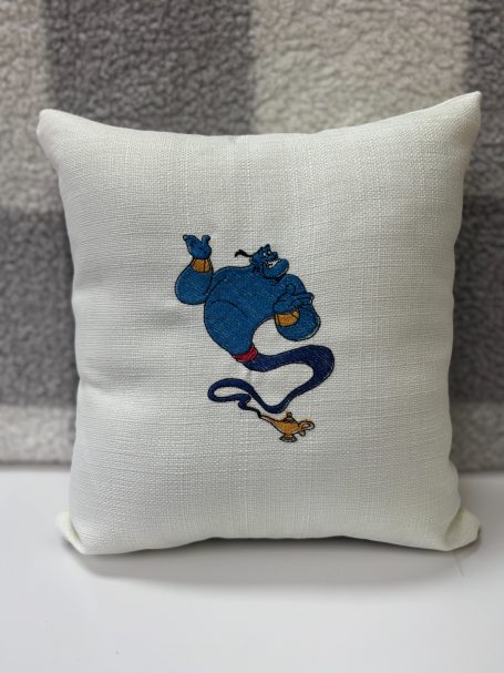 A small cushion featuring an embroidered blue genie character.