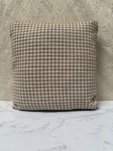 Square cushion with a brown and white checked pattern on a light surface.