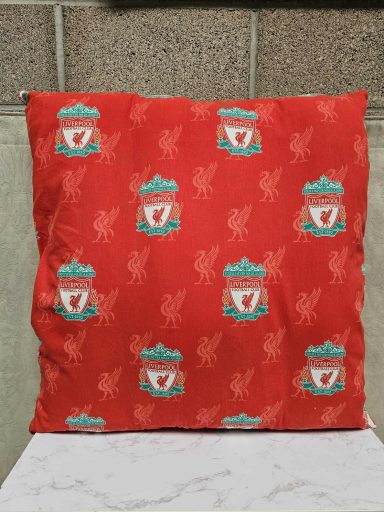 A red cushion featuring the Liverpool FC crest and decorative elements.