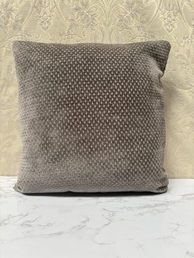 Square, textured grey cushion on a marble surface against a patterned background.