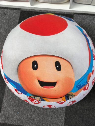 Round cushion featuring a smiling character with a large white hat and red spot.