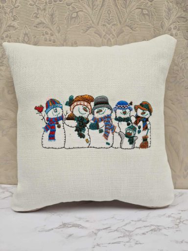 Embroidered cushion featuring four cheerful snowmen in winter attire.