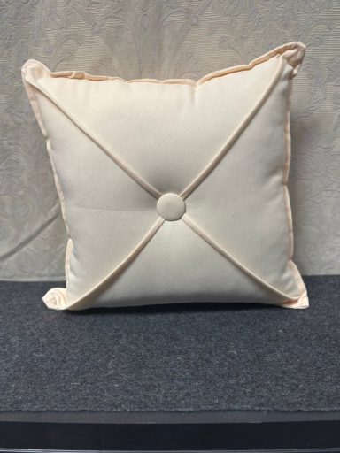 Square cream cushion with a central button and cross-stitch detailing.