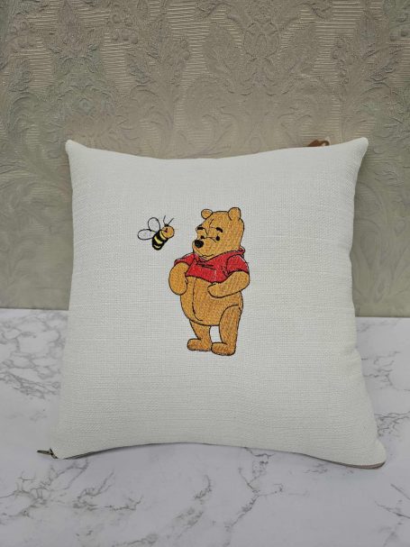 A cushion featuring Winnie the Pooh with a bee flying nearby.