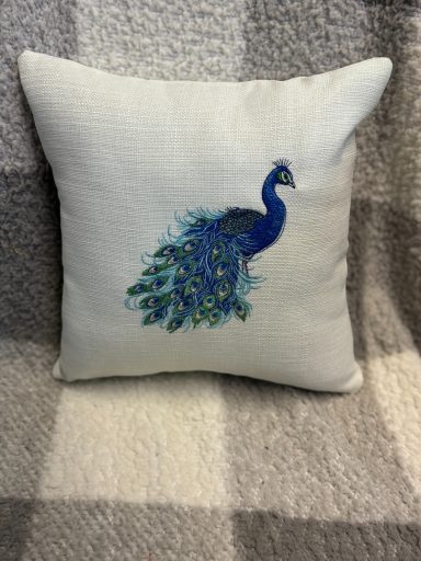 Square cushion featuring a blue peacock design on a light background.