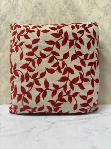 A decorative cushion with a cream background and red leaf pattern.