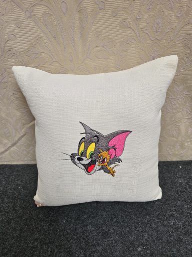 A decorative pillow featuring a smiling cartoon cat with a small mouse.
