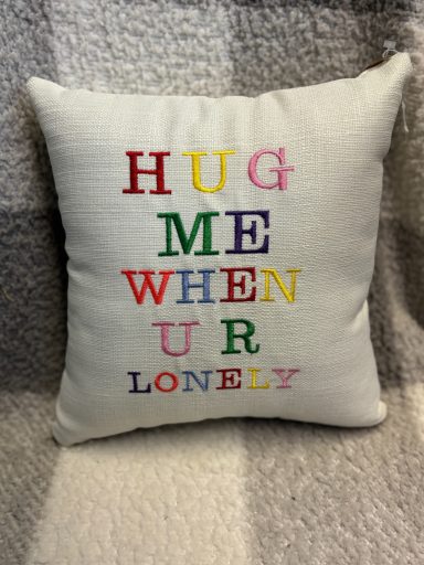 Cushion with colourful lettering: "HUG ME WHEN UR LONELY".