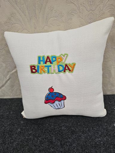 White cushion featuring "Happy Birthday" in colourful letters and a cupcake design.