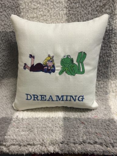 Cushion featuring an embroidered girl and frog with the word "DREAMING".