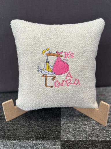 A decorative cushion featuring a stork and the text "It's a girl."