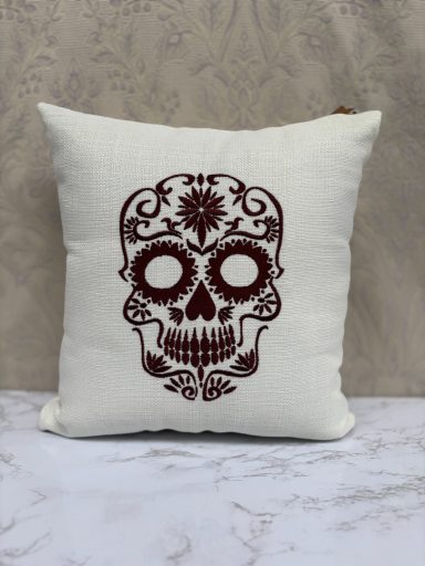 Cushion with a maroon sugar skull design on a cream background.