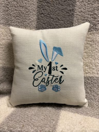 Decorative cushion with "My 1st Easter" text and bunny motifs.