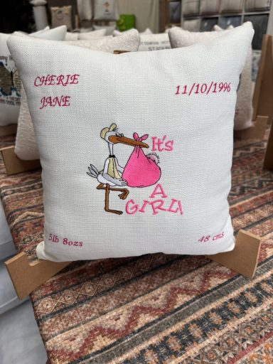 Decorative cushion featuring a stork and embroidered text celebrating a baby's birth.