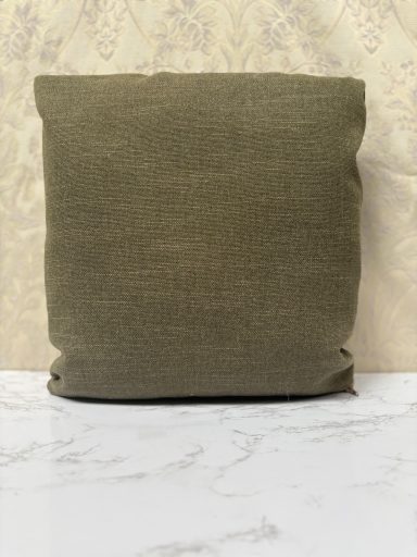 Plain green cushion against a patterned wallpaper background.
