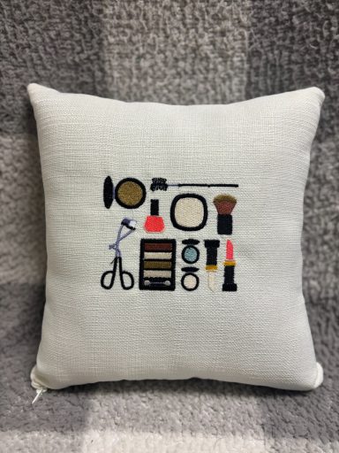 A decorative cushion featuring various sewing and makeup items illustrated on it.