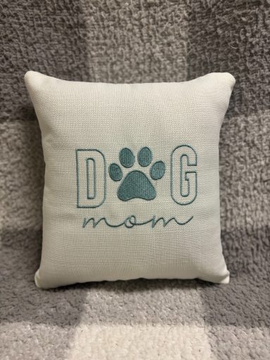 Square cushion with "DOG mom" text and a paw print design in teal on a light background.