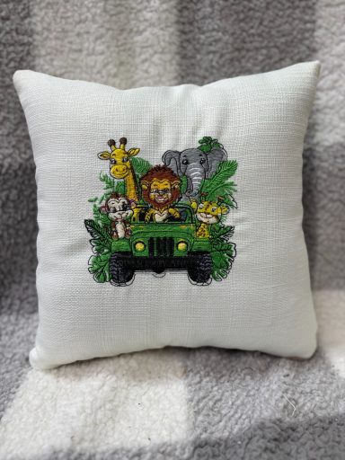 Embroidered cushion featuring a lion, giraffe, and elephant in a green jeep surrounded by foliage.
