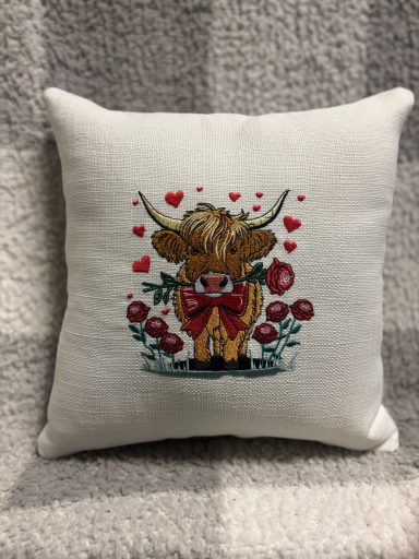 Decorative cushion featuring a cow with a bow, surrounded by roses and hearts.