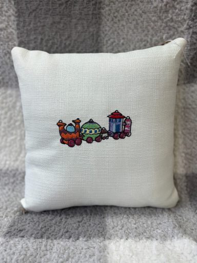 White cushion featuring embroidered colourful train and houses design.