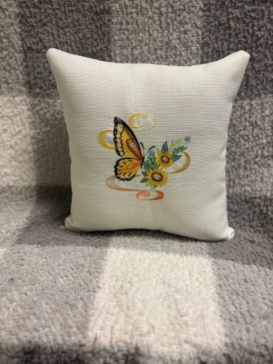 Decorative cushion featuring a butterfly and floral embroidery on a light background.