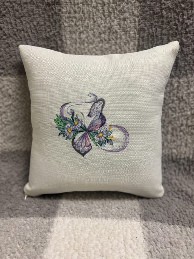 Decorative cushion with embroidered purple flowers and green leaves on a light background.