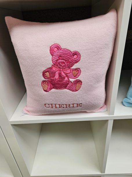 Pink cushion with a teddy bear design and the word "Cuddles" beneath it.