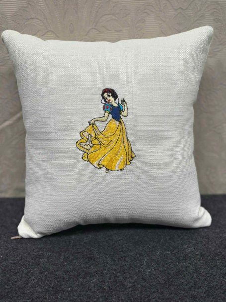 Cushion featuring an embroidered illustration of Snow White in a yellow dress.