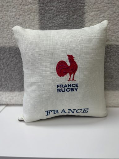 White cushion featuring a red embroidered rooster and the text "RUGBY FRANCE."